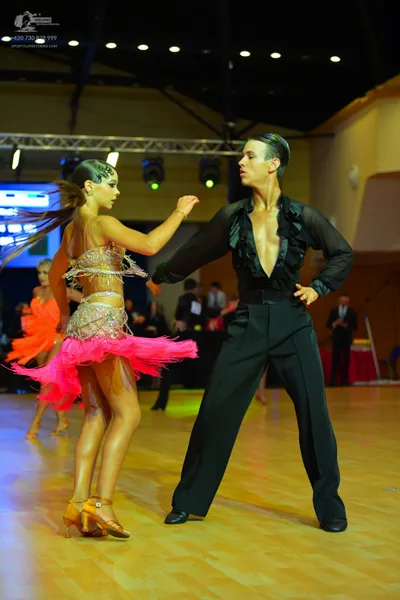Dancesport competitor: Female dancer: gold sequined top and vibrant pink fringed Latin dress with gold 