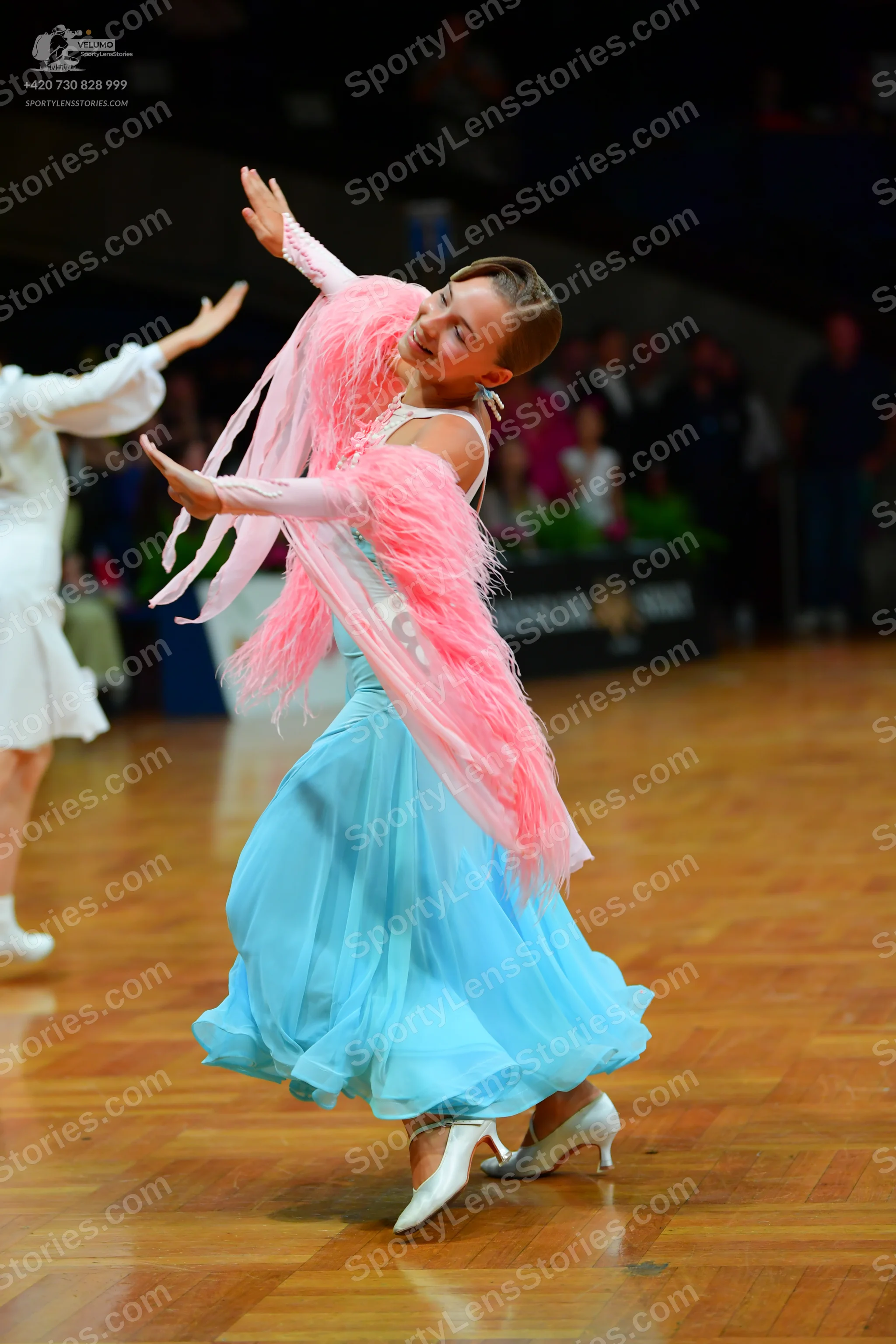 Dancesport competitor: Female dancer: light blue ballgown with a flowing skirt and a large, long pink f