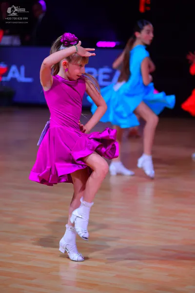 Dancesport competitor: Female dancer 1: magenta latin dress with a ruffled skirt and a matching flower 