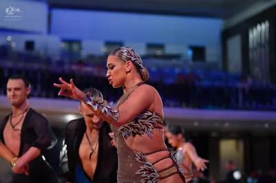 Dancesport competitor: Foreground female dancer: tan/nude Latin dance costume featuring intricate dark,