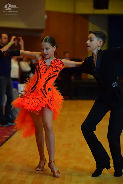 Dancesport competitor: Female dancer: bright orange Latin dance dress with black sequin patterns and or