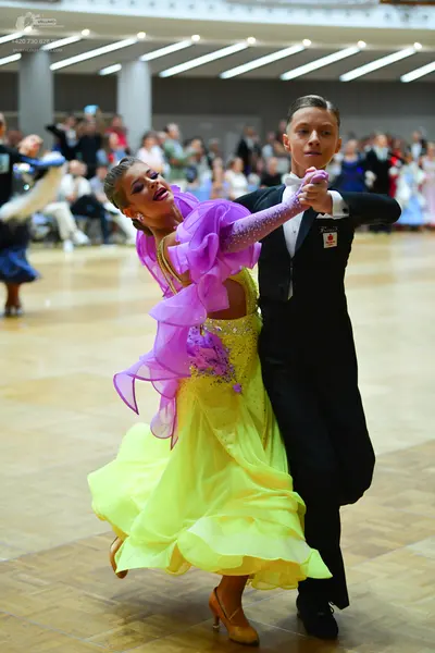 Dancesport competitor: Female dancer: yellow ballgown with large purple ruffles and a long purple sequi