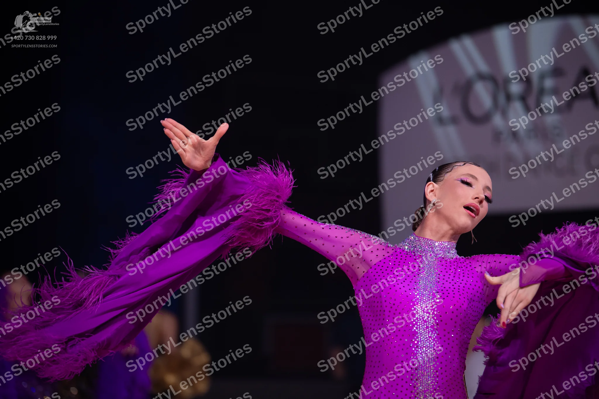 Dancesport competitor: Female dancer: magenta long-sleeved dress with sequins and large, feathery sleev