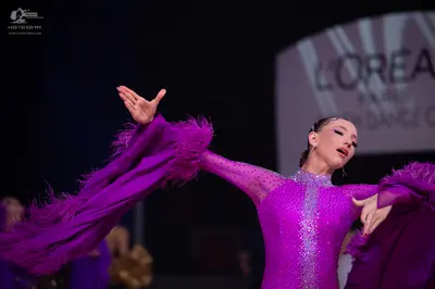 Dancesport competitor: Female dancer: magenta long-sleeved dress with sequins and large, feathery sleev