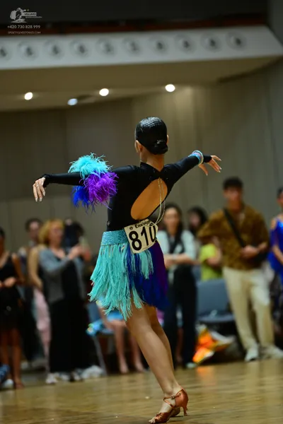 Dancesport competitor #810: Female dancer: black Latin dance costume with long fringe in cyan, blue, and pur