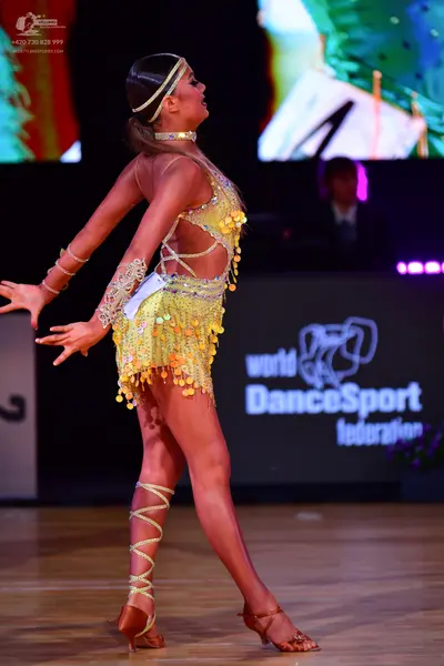 Dancesport competitor: Female dancer: gold/yellow latin dance costume featuring sequins, cutouts, and g