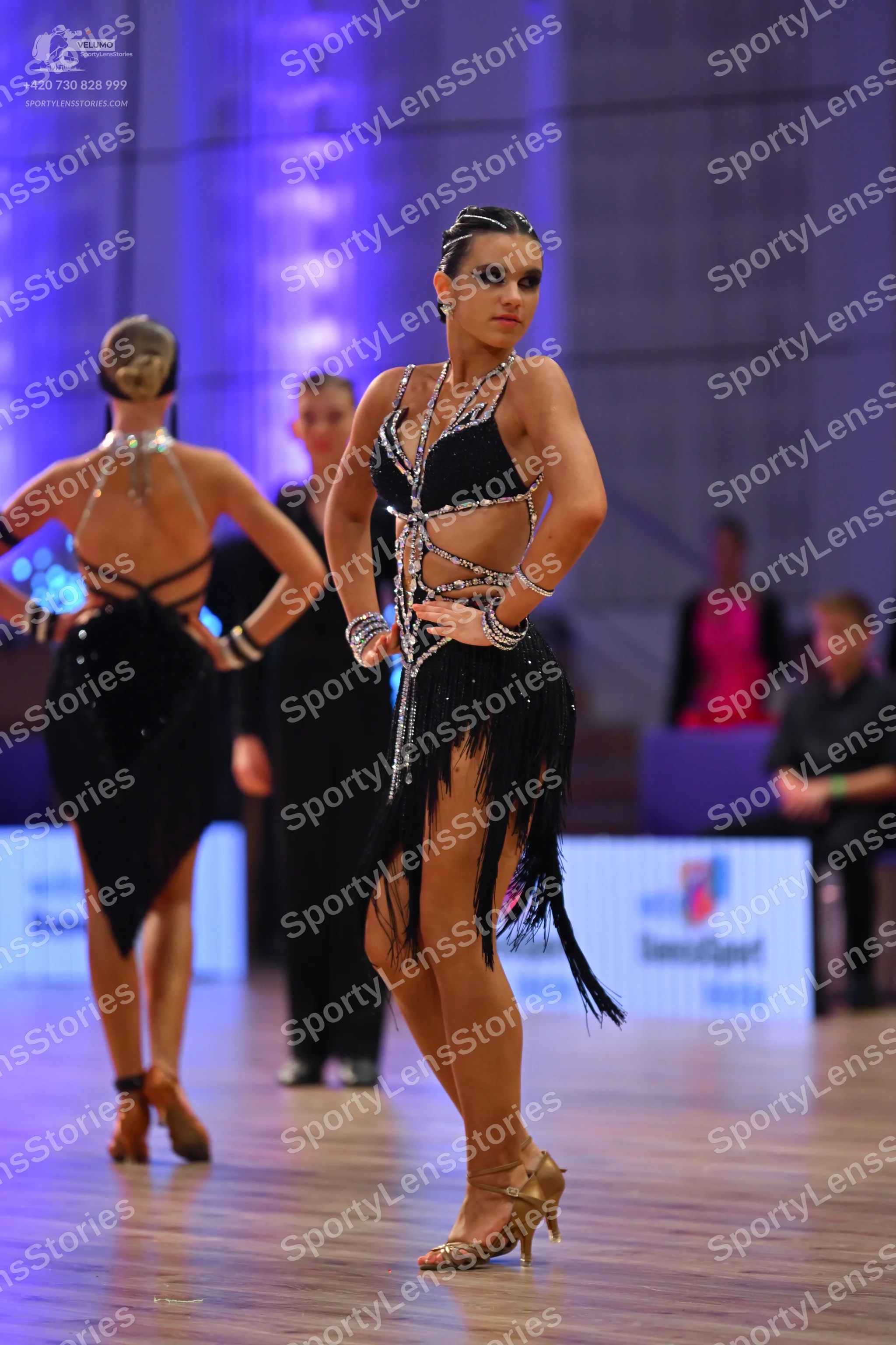 Dancesport competitor: Female dancer in foreground: black latin dress with silver rhinestone-embellishe