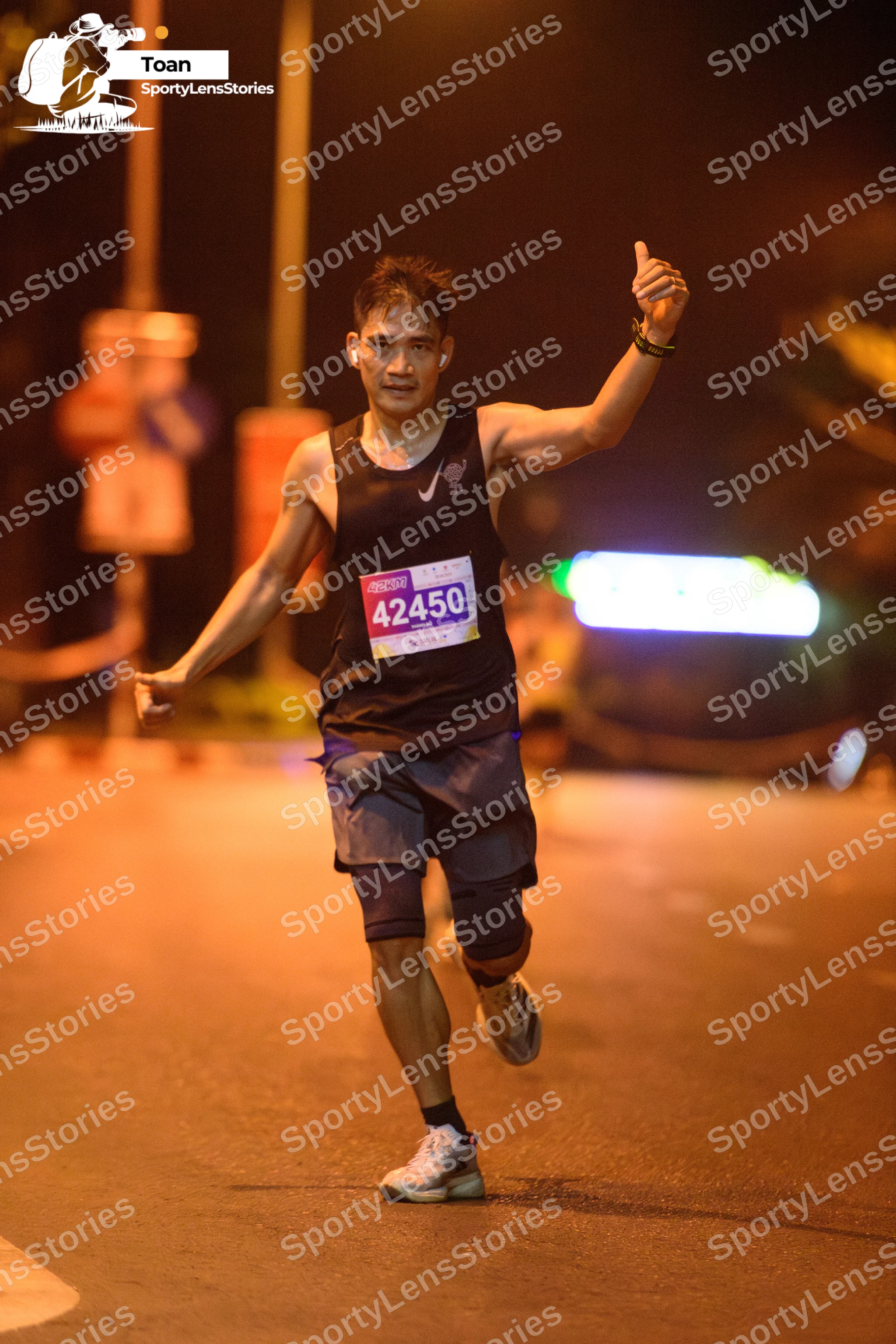 Marathon runner #42450: Runner 1: black tank top, dark grey shorts, white running shoes, and a black wri