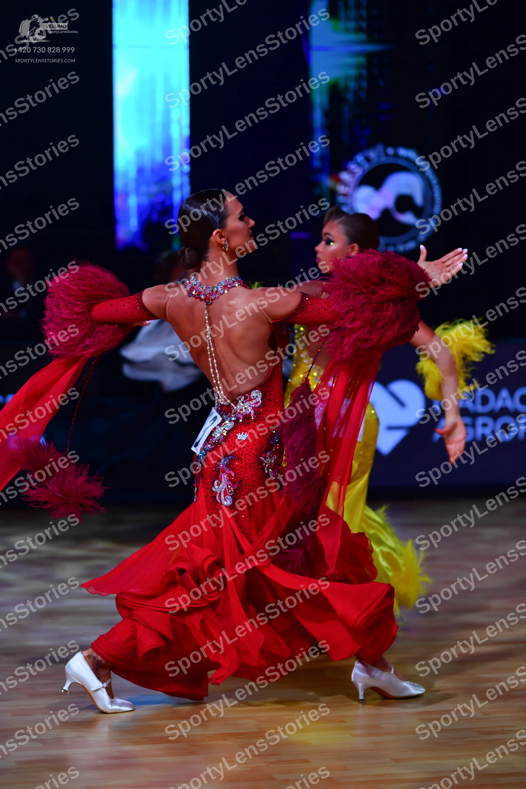 Dancesport competitor: Female dancer 1: red latin dress with large red feather trim on the arms, a ruff
