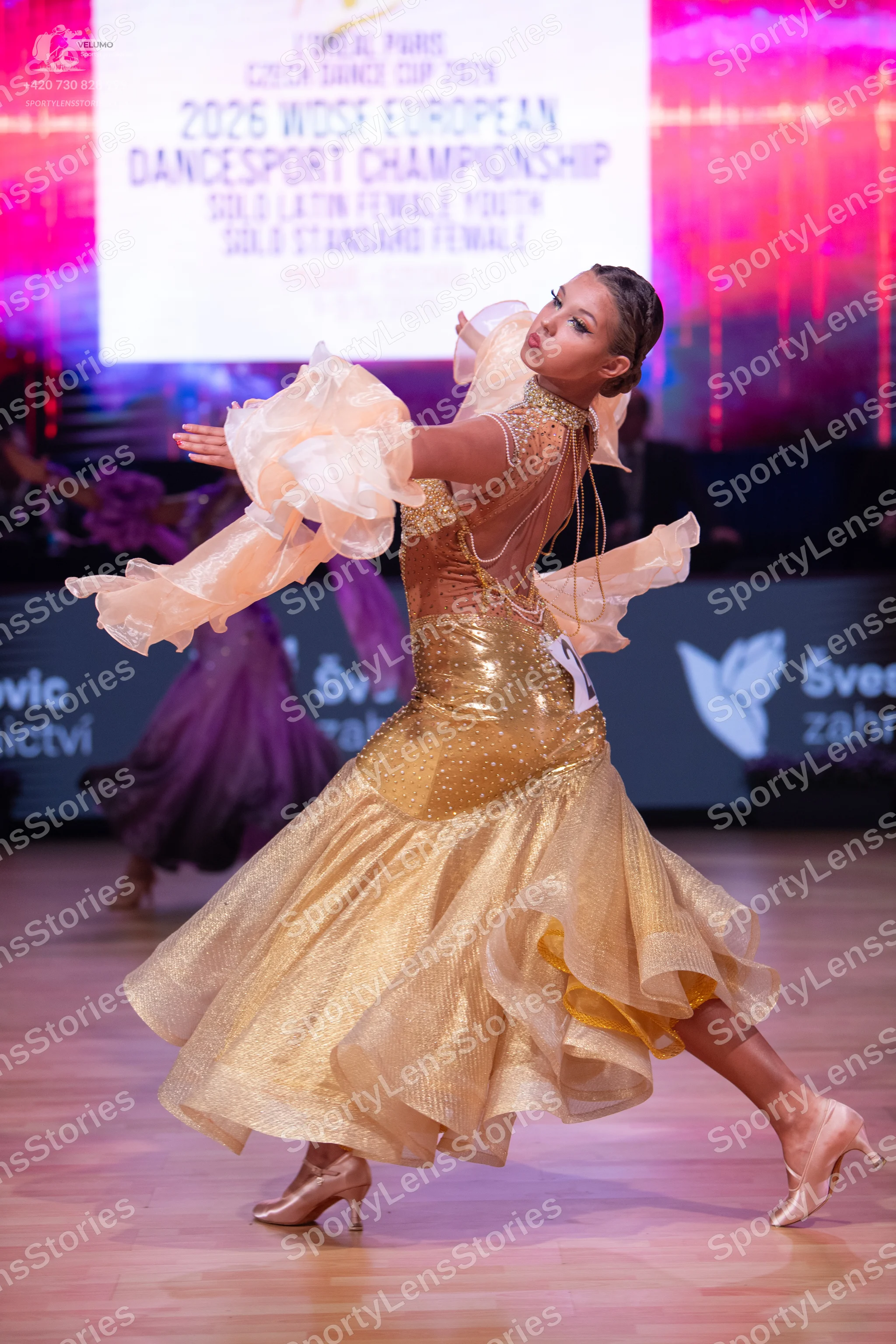 Dancesport competitor: Female dancer: gold latin dress with a shimmering, multi-layered, ruffled skirt,