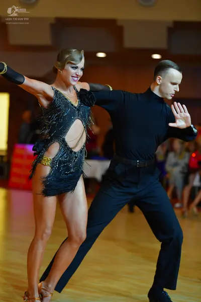 Dancesport competitor: Female dancer: Black Latin dance dress featuring fringe, cut-outs, and long slee