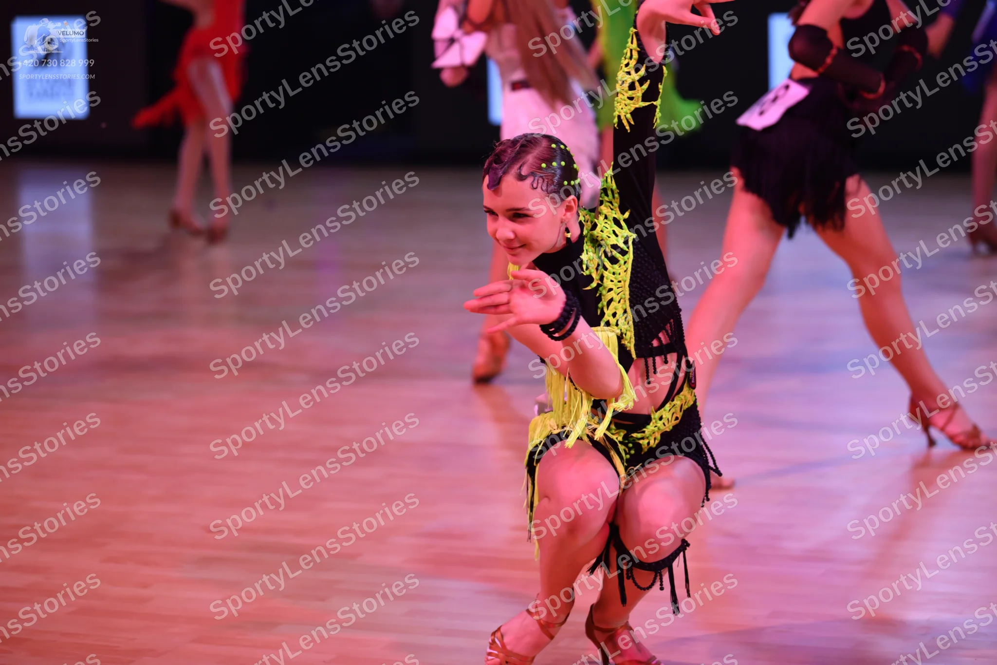 Dancesport competitor: Foreground female dancer: black latin dance costume with neon lime green accents