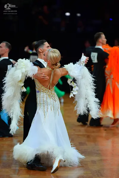 Dancesport competitor #10: Foreground female dancer: white ballgown with a gold and silver sequined bodice,