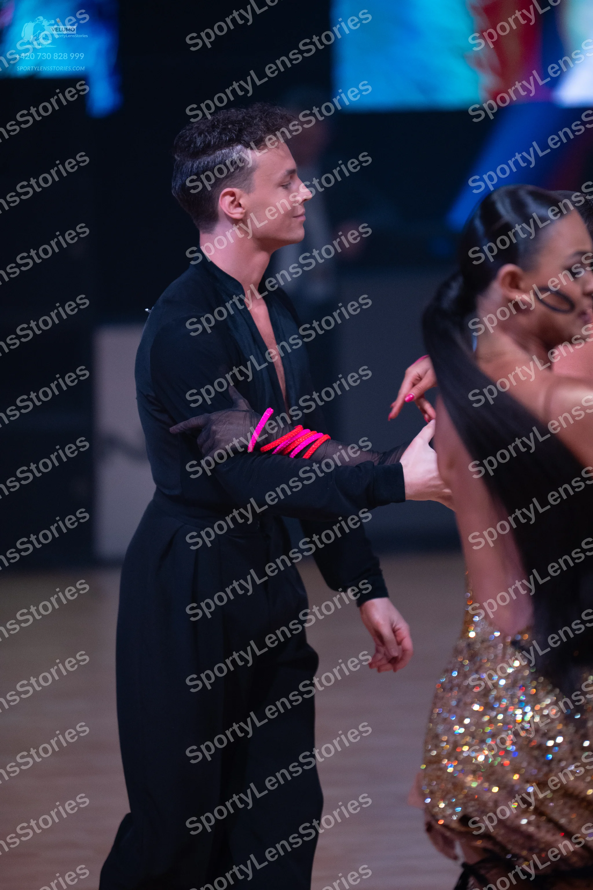Dancesport competitor: Male dancer: black long-sleeved top and trousers with pink/red accents on his sl