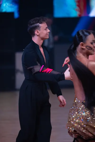 Dancesport competitor: Male dancer: black long-sleeved top and trousers with pink/red accents on his sl