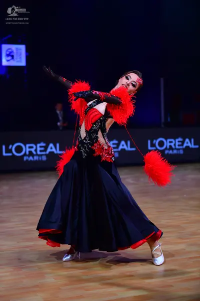 Dancesport competitor: Female dancer: black ballroom dress with red accents, featuring a lace-patterned