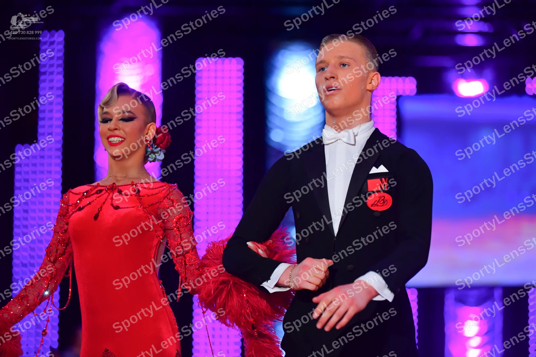 Dancesport competitor: Male dancer: black suit with a white shirt, white bowtie, and a red circular pin