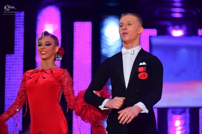 Dancesport competitor: Male dancer: black suit with a white shirt, white bowtie, and a red circular pin