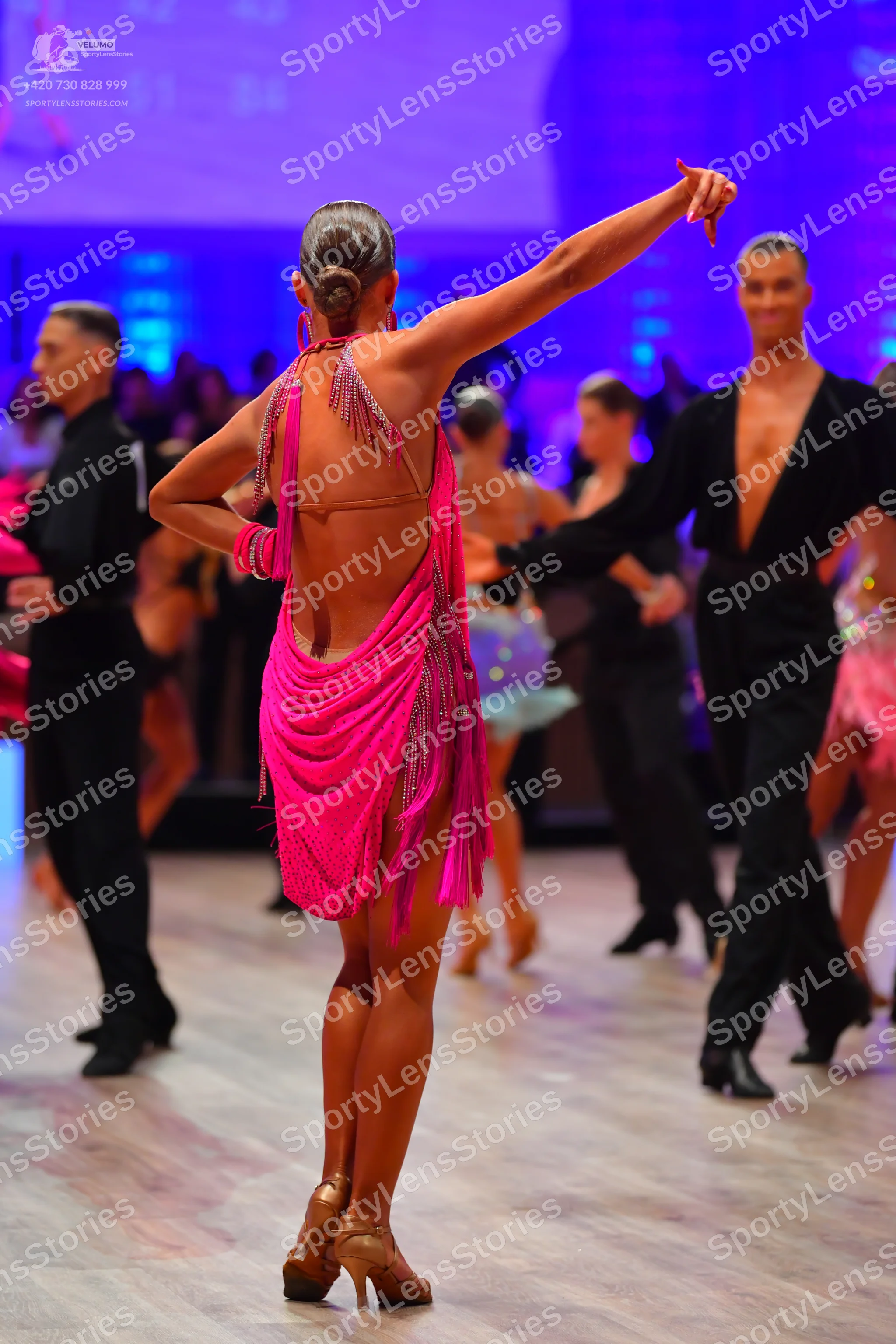 Dancesport competitor: Female dancer in foreground: bright pink Latin dress with long fringe and sequin