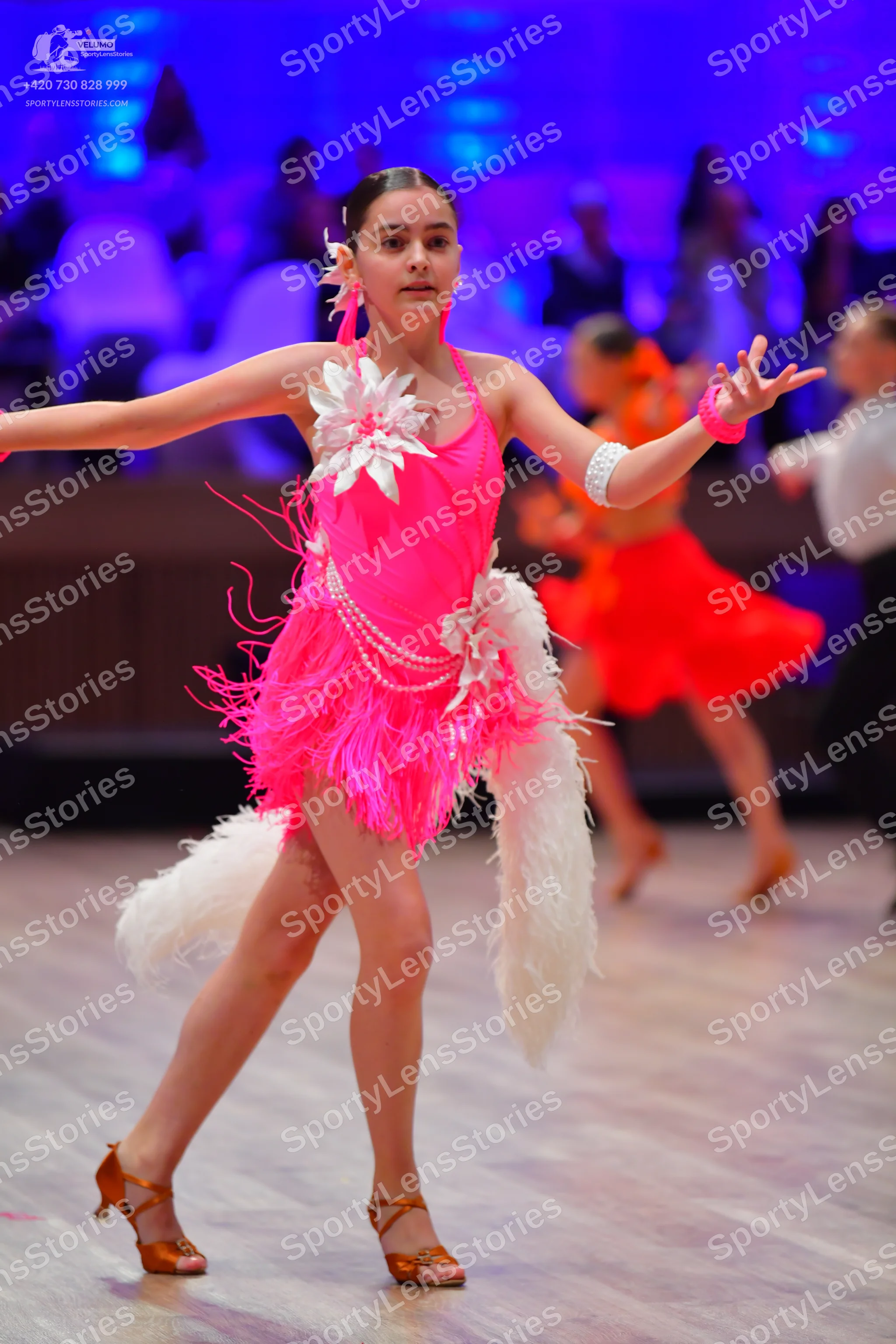 Dancesport competitor: Female dancer in foreground: bright pink Latin dance dress with white floral emb