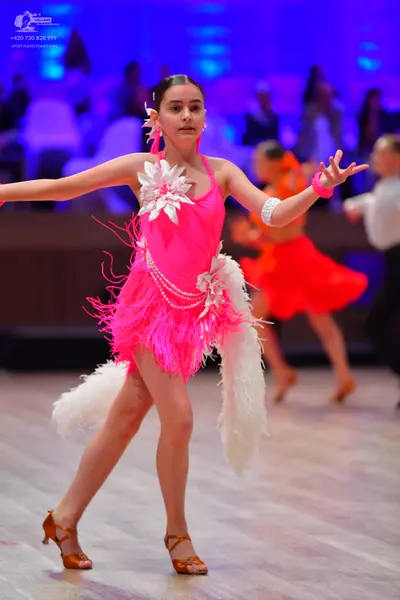Dancesport competitor: Female dancer in foreground: bright pink Latin dance dress with white floral emb