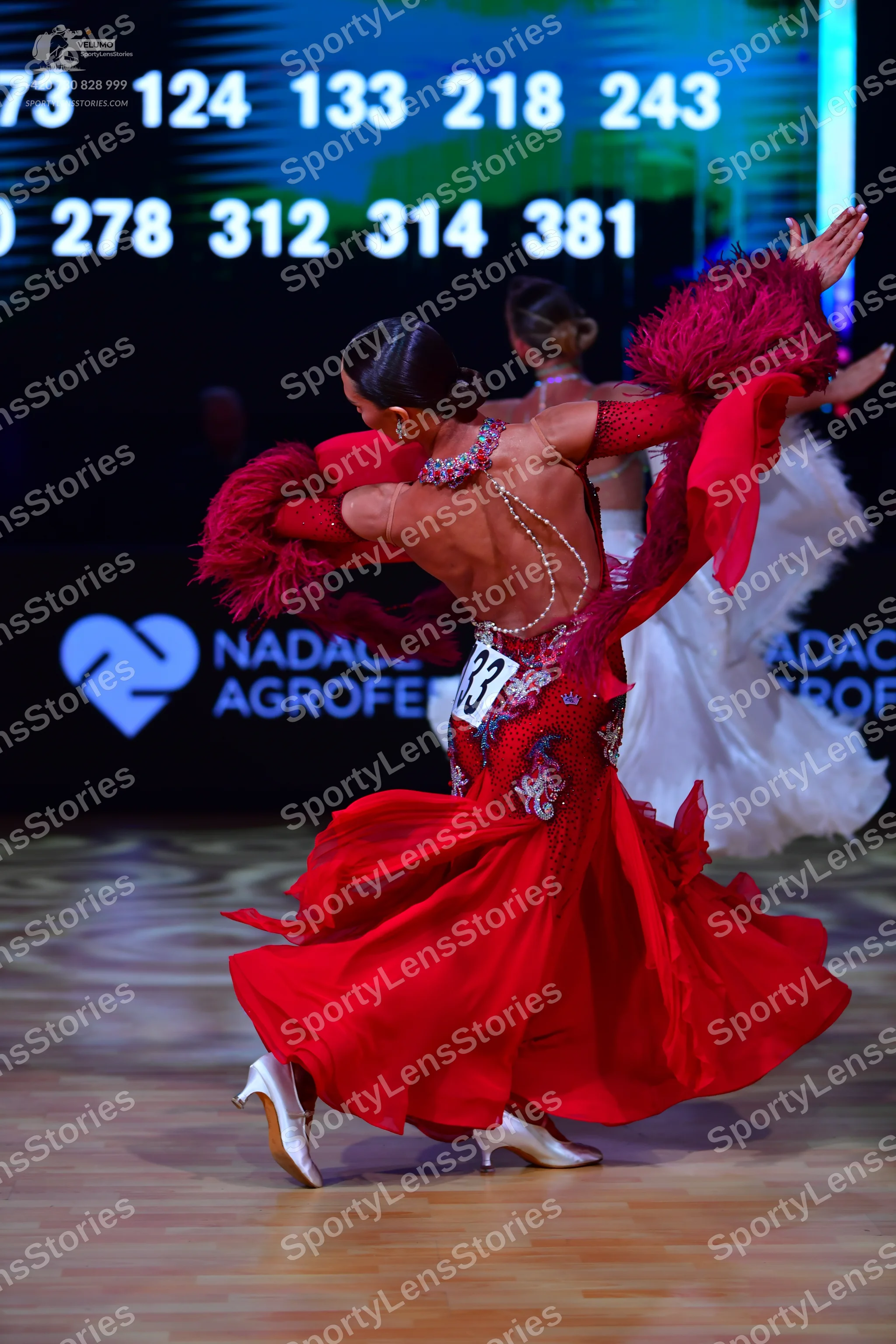 Dancesport competitor: Female dancer: red latin dress with red feather trim on the sleeves and beaded/s