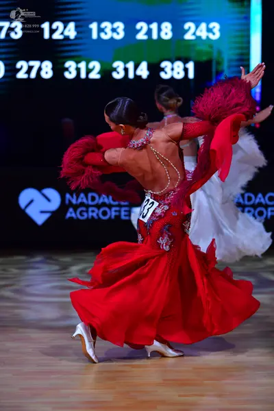 Dancesport competitor: Female dancer: red latin dress with red feather trim on the sleeves and beaded/s