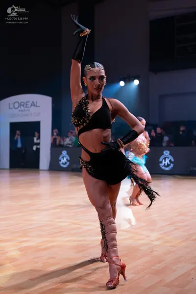 Dancesport competitor: Female dancer in foreground: black latin dance costume with gold sequin embellis