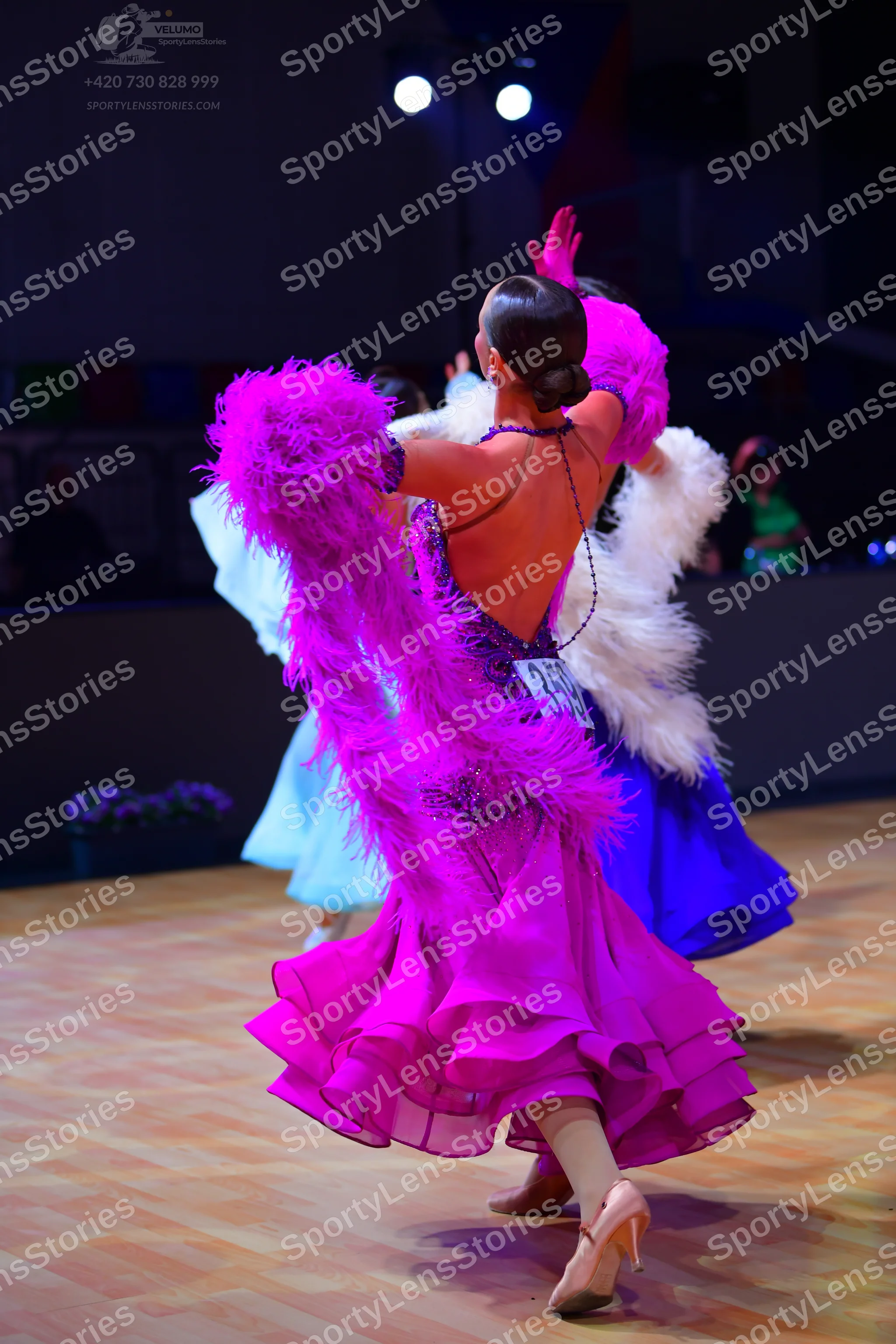 Dancesport competitor: Female dancer in foreground: bright pink/magenta ballroom dress with voluminous