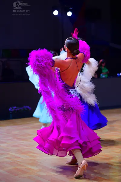 Dancesport competitor: Female dancer in foreground: bright pink/magenta ballroom dress with voluminous 