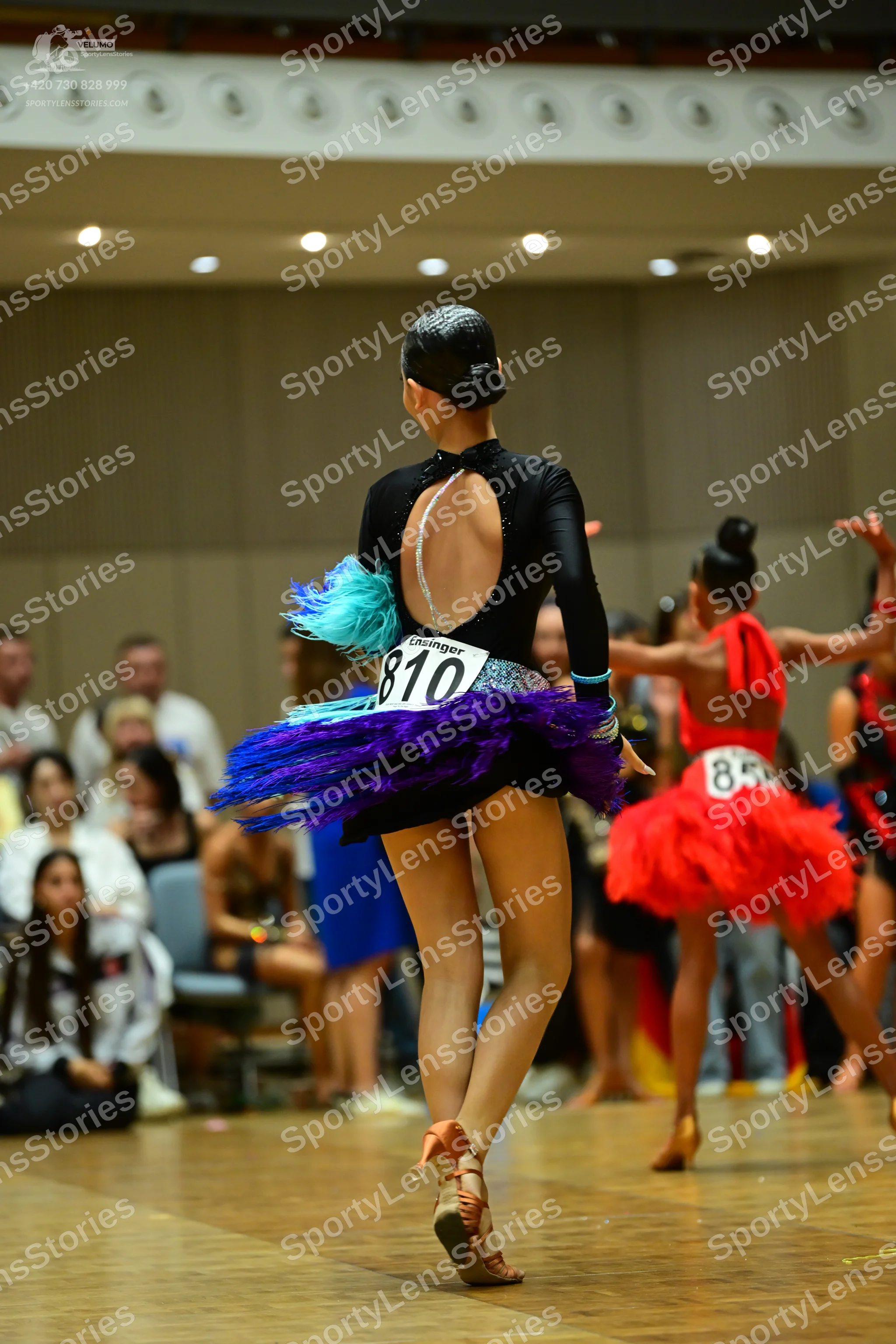 Dancesport competitor #810, #85: First dancer: black long-sleeved top with a keyhole back cutout and a multi-colo