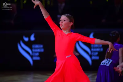 Dancesport competitor: Female dancer in foreground: bright red long-sleeved Latin dress