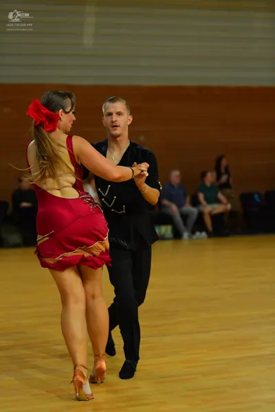 Dancesport competitor: Female dancer: red latin dress with gold decorative patterns and a red flower in