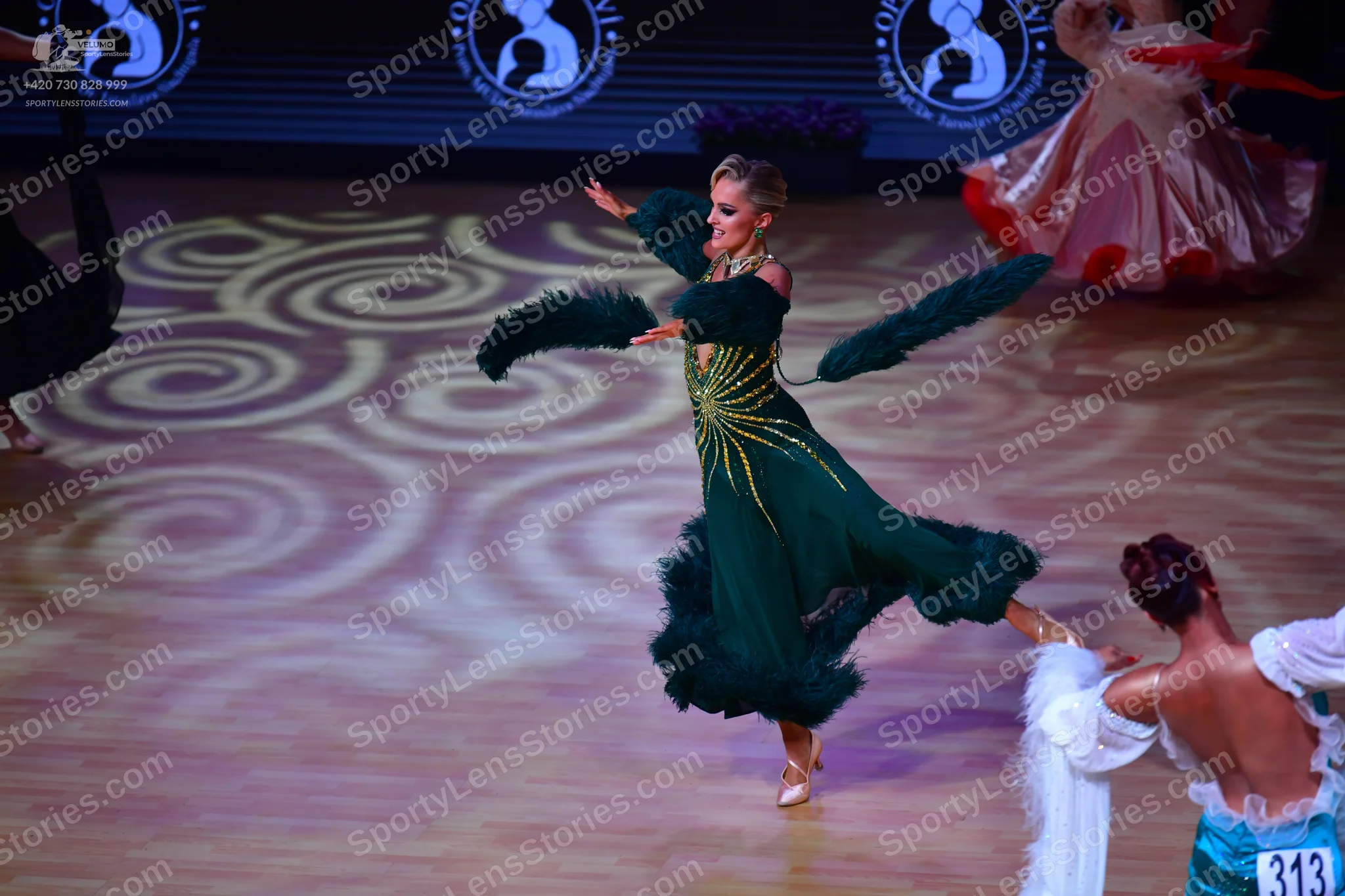 Dancesport competitor: Female dancer (center): emerald green Latin dress with dark green feathered or f