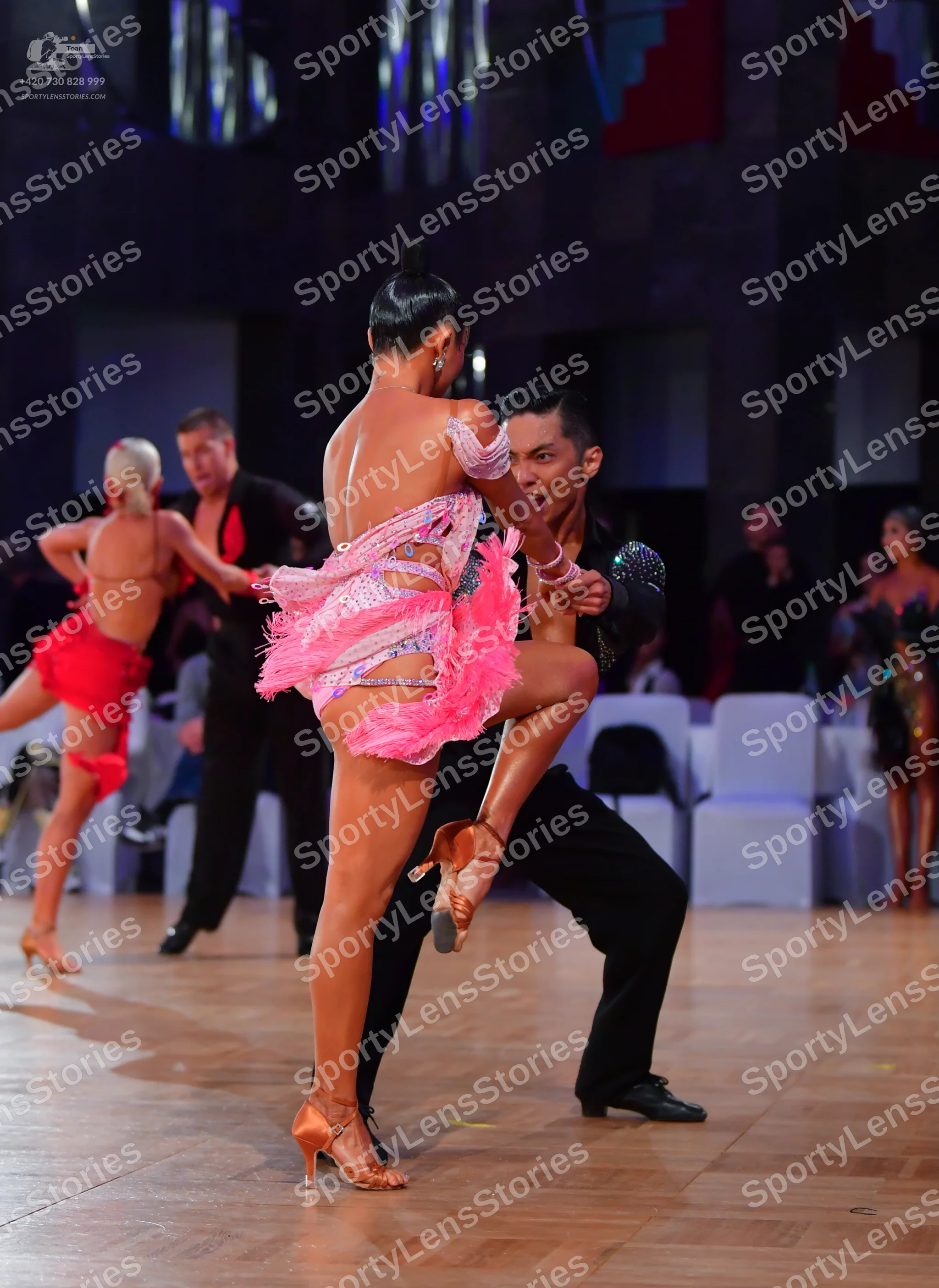Dancesport competitor: Foreground female dancer: pink latin dress with sequins and pink feather/fringe