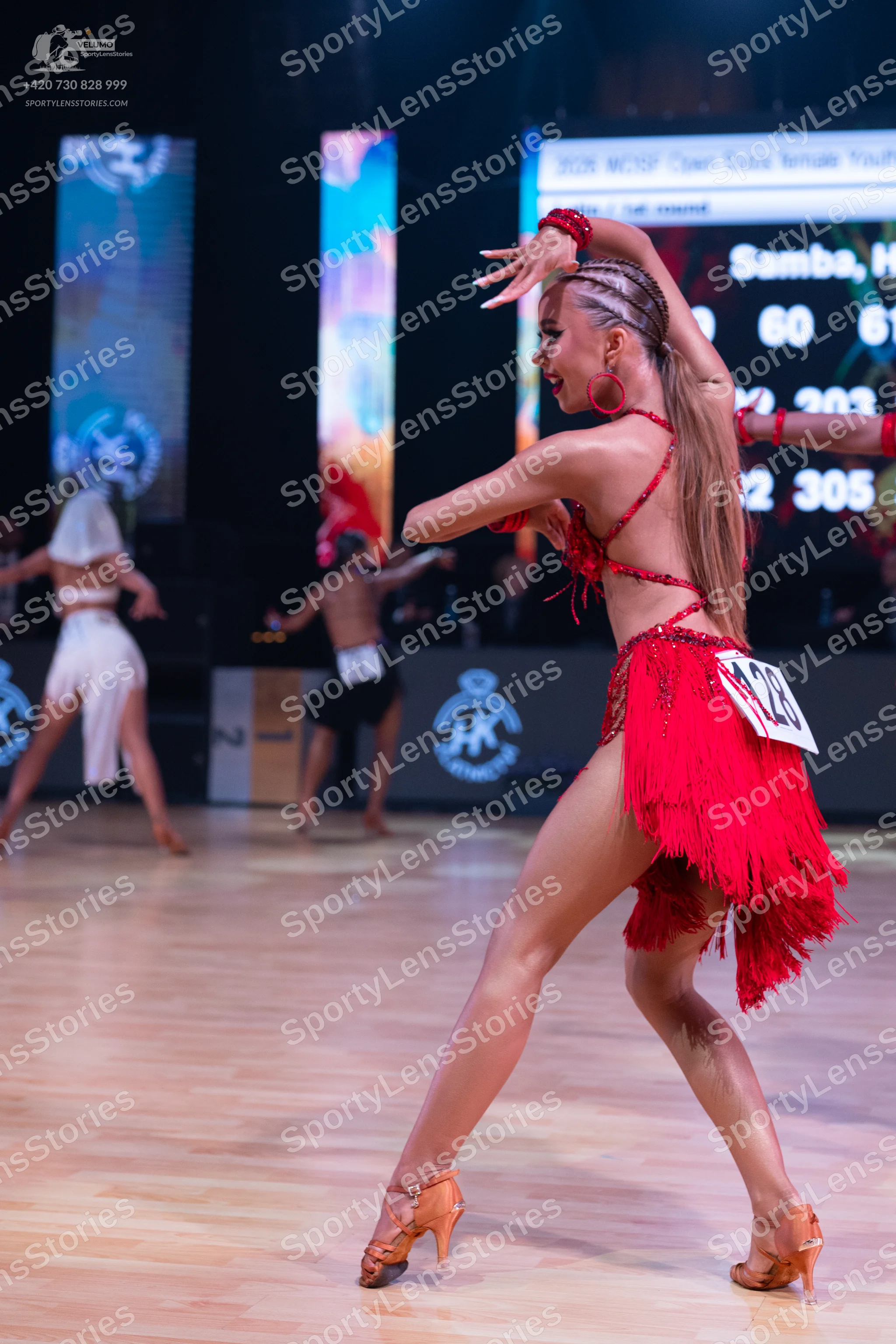 Dancesport competitor: Female dancer in foreground: red latin dress with fringe and red earrings
