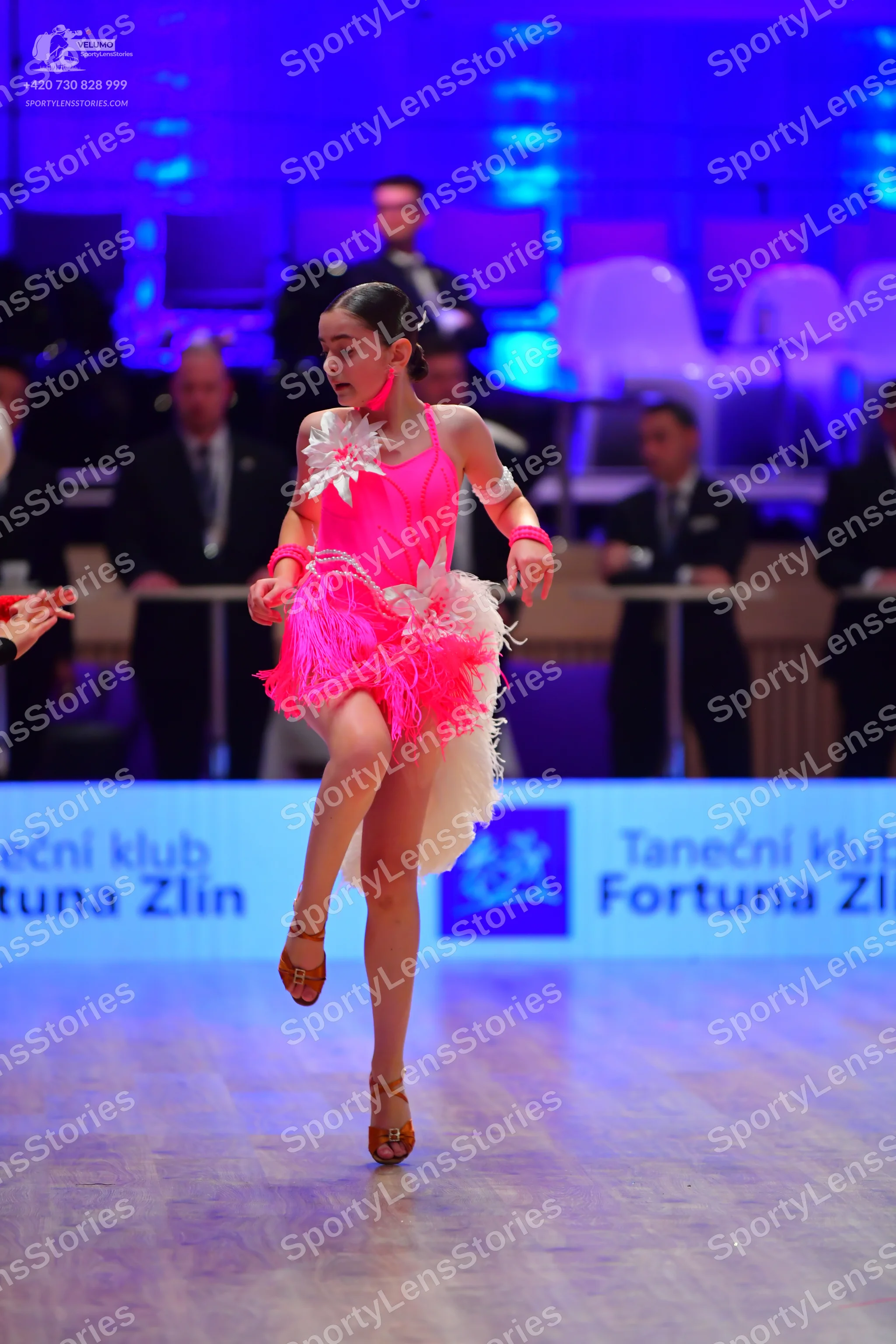 Dancesport competitor: Female dancer: bright pink Latin dress with a sequined bodice, a large white flo