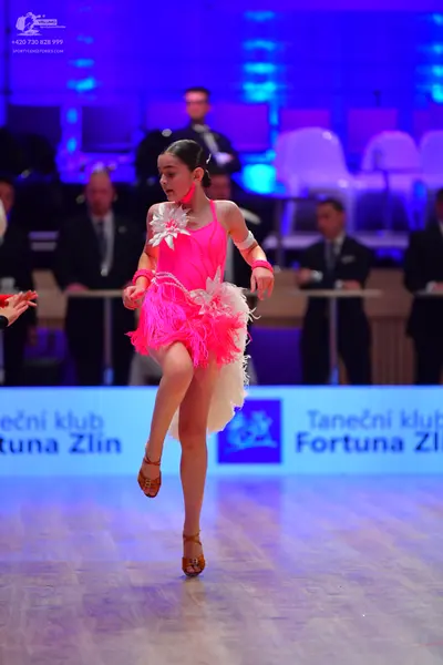 Dancesport competitor: Female dancer: bright pink Latin dress with a sequined bodice, a large white flo
