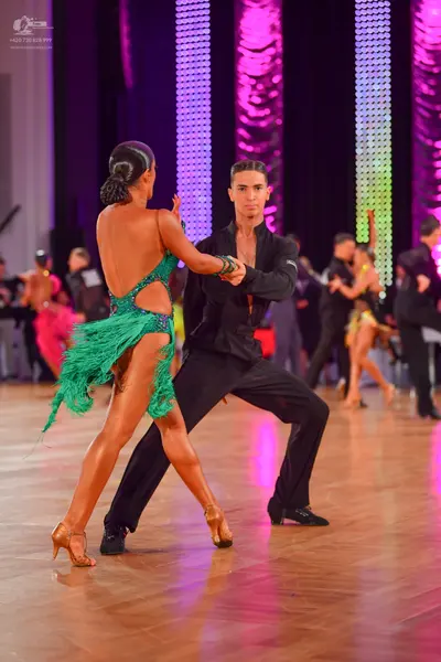 Dancesport competitor: Female dancer in foreground: green latin dress with sequins and long fringe