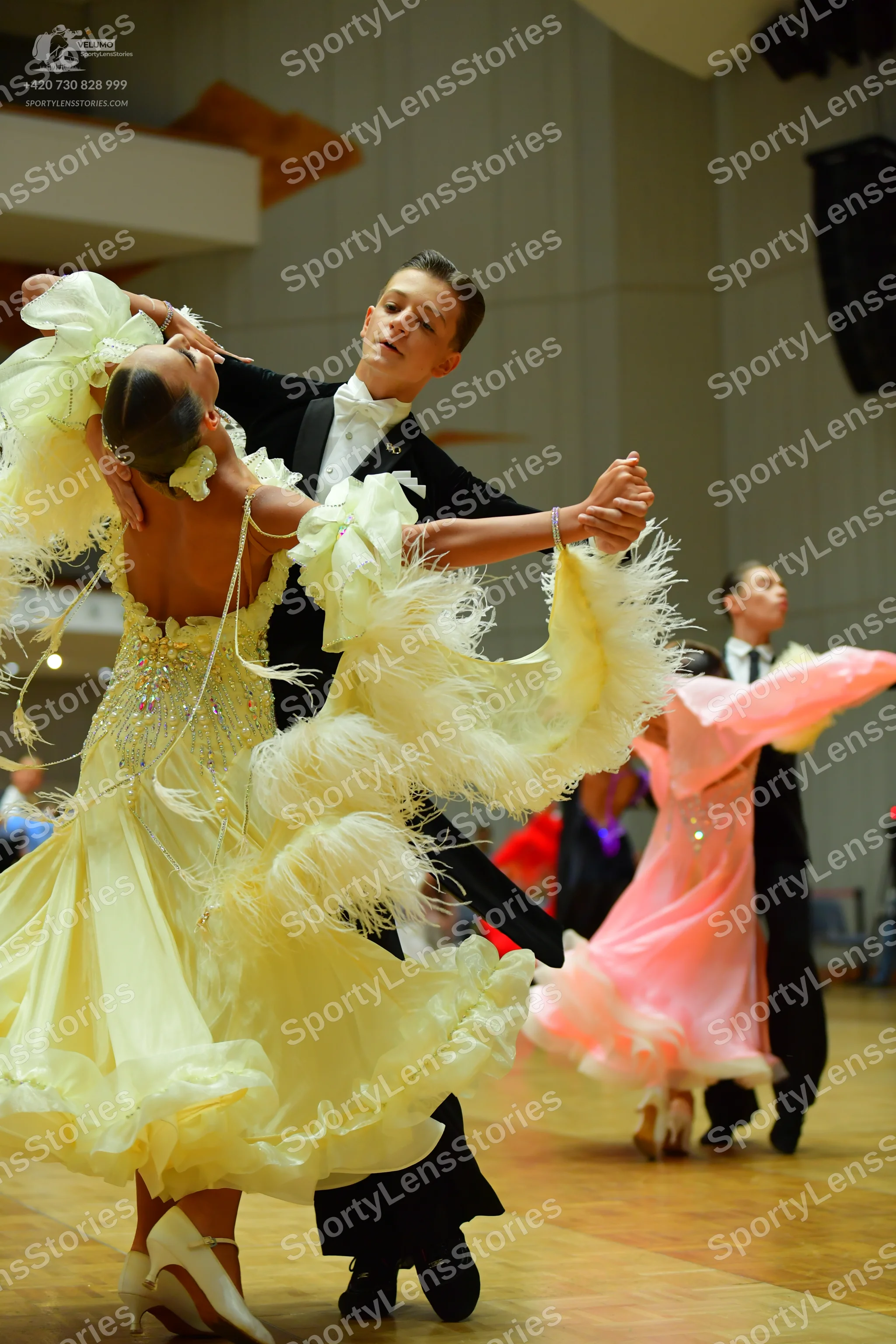 Dancesport competitor: Female dancer in foreground: voluminous yellow ballgown with ruffled layers and