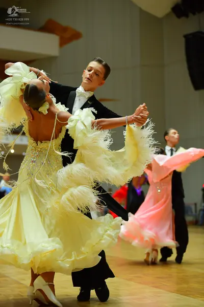 Dancesport competitor: Female dancer in foreground: voluminous yellow ballgown with ruffled layers and 