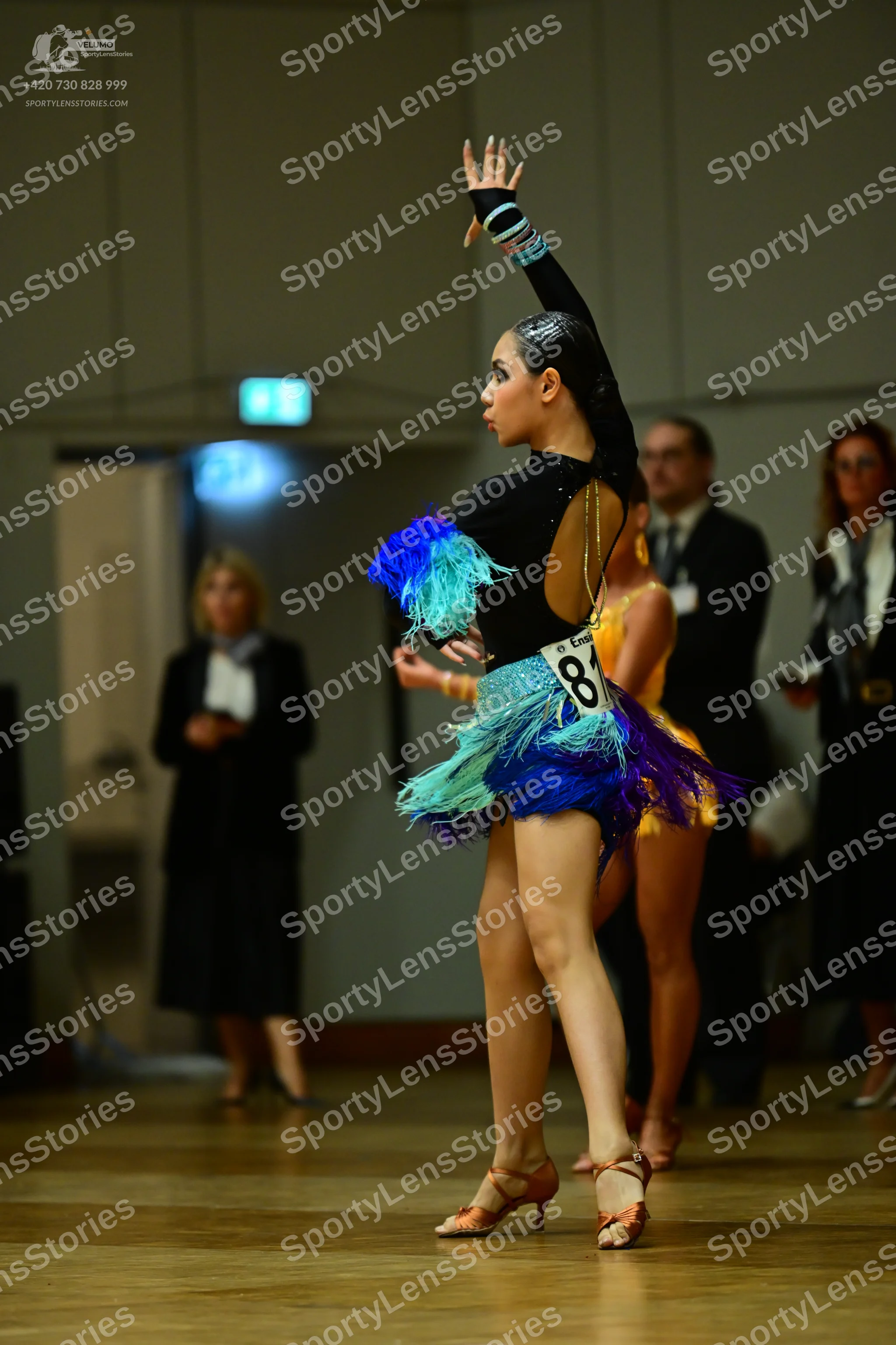 Dancesport competitor: Female dancer: black latin dress with long sleeves, an open back, and colorful f