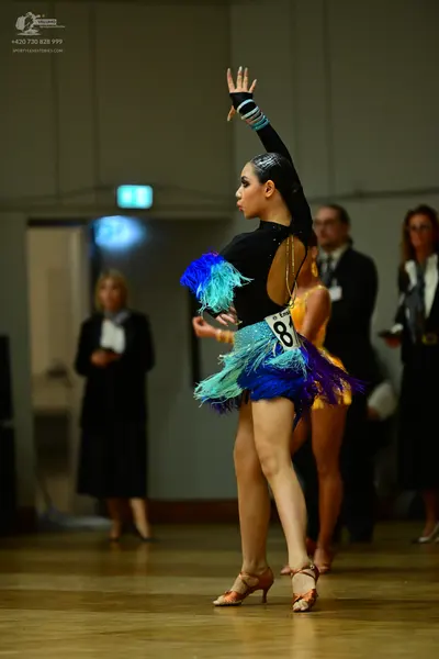 Dancesport competitor: Female dancer: black latin dress with long sleeves, an open back, and colorful f