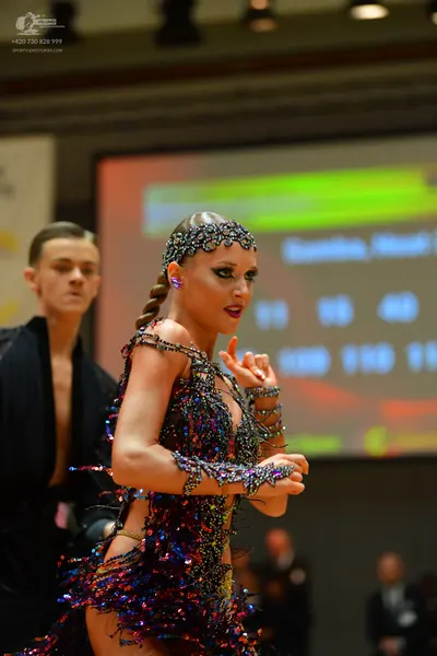 Dancesport competitor: Female dancer: dark-colored Latin dance dress heavily embellished with multi-col