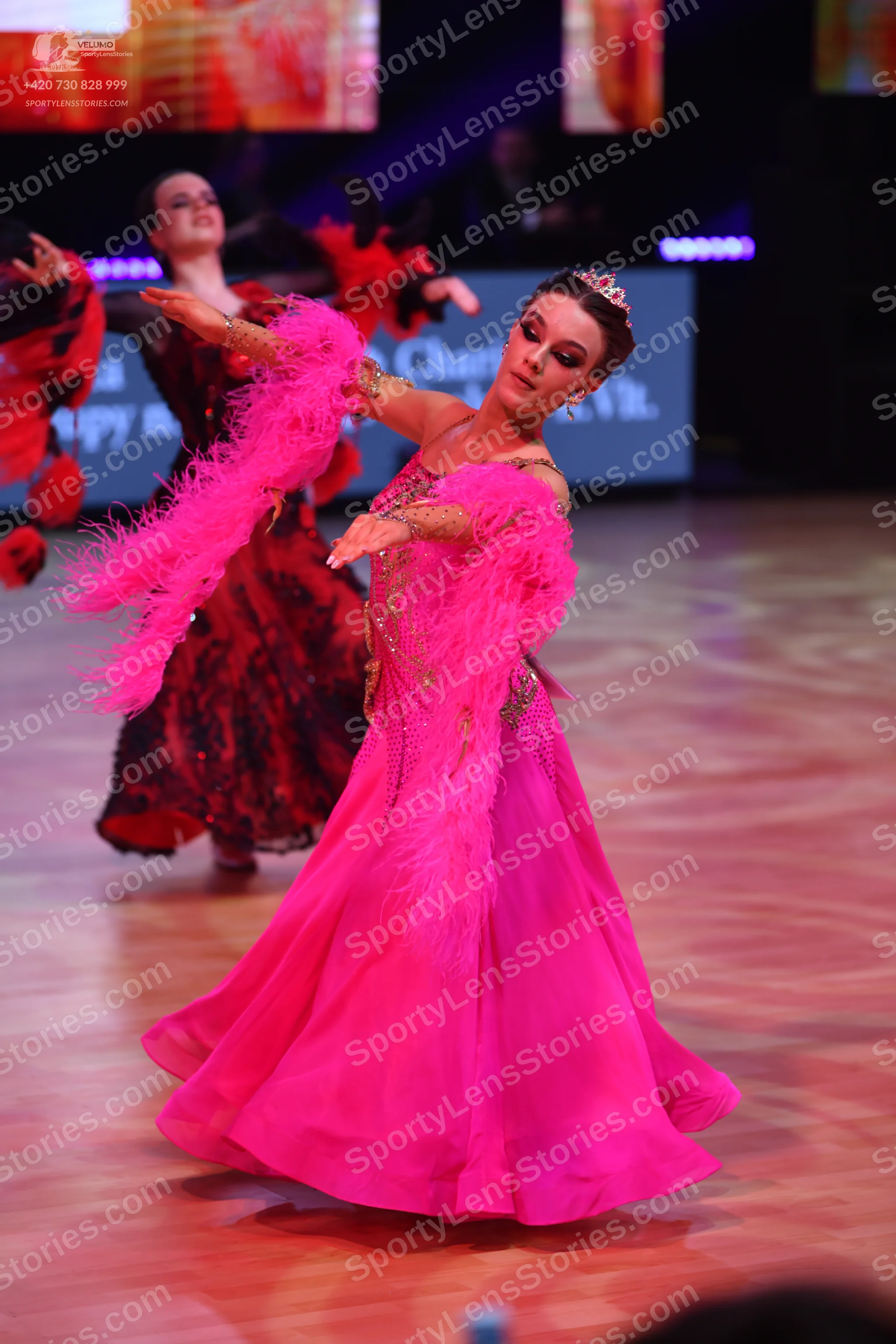 Dancesport competitor: Female dancer in foreground: bright pink ballgown with large pink feather accent