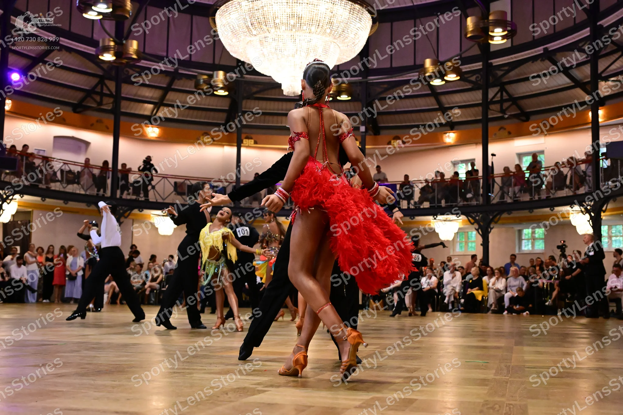 Dancesport competitor: Female dancer in foreground: red latin dress with ruffled or fringed layers