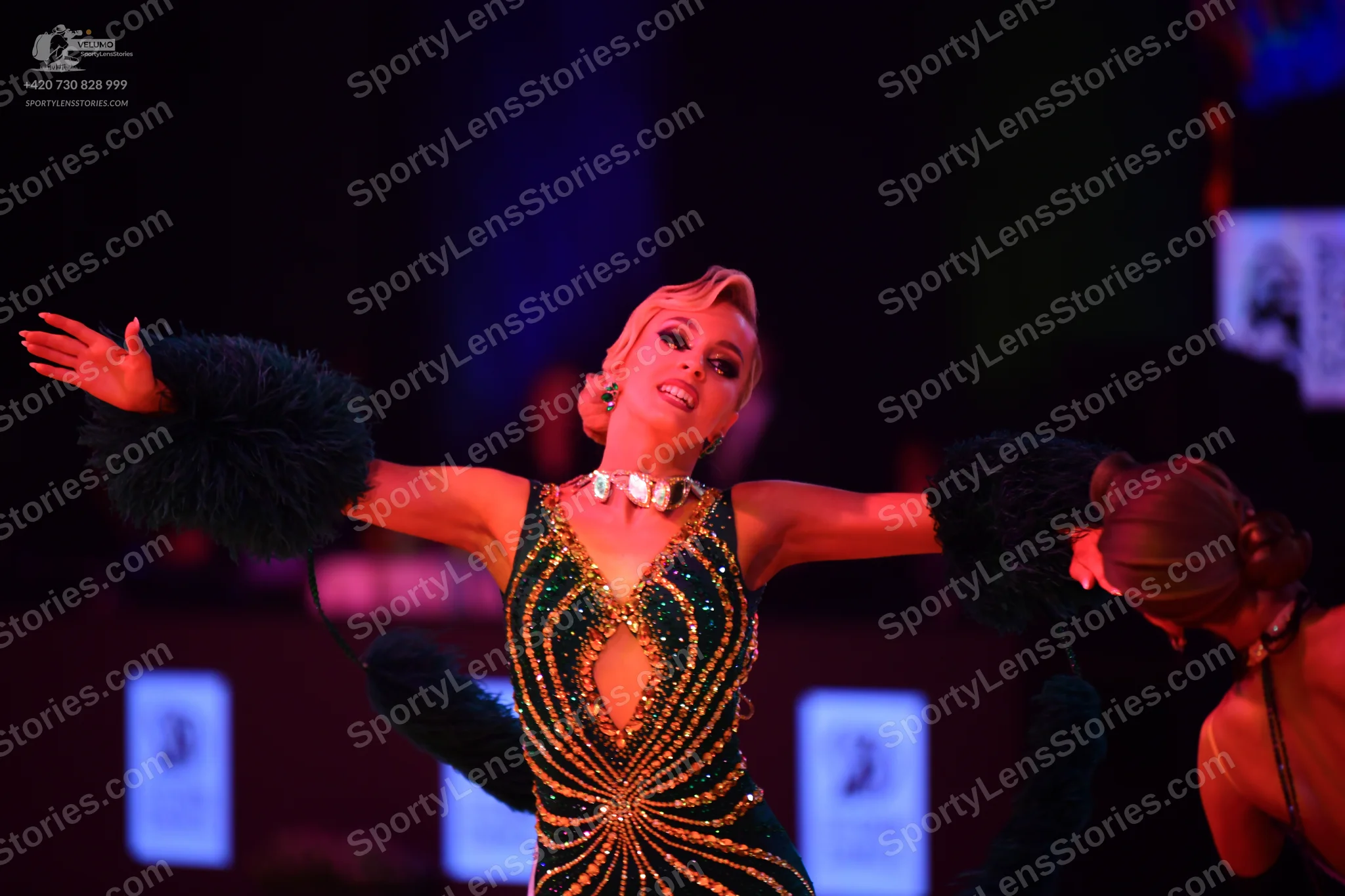 Dancesport competitor: Female dancer: dark green/black Latin dress with gold sequin sunburst pattern, a