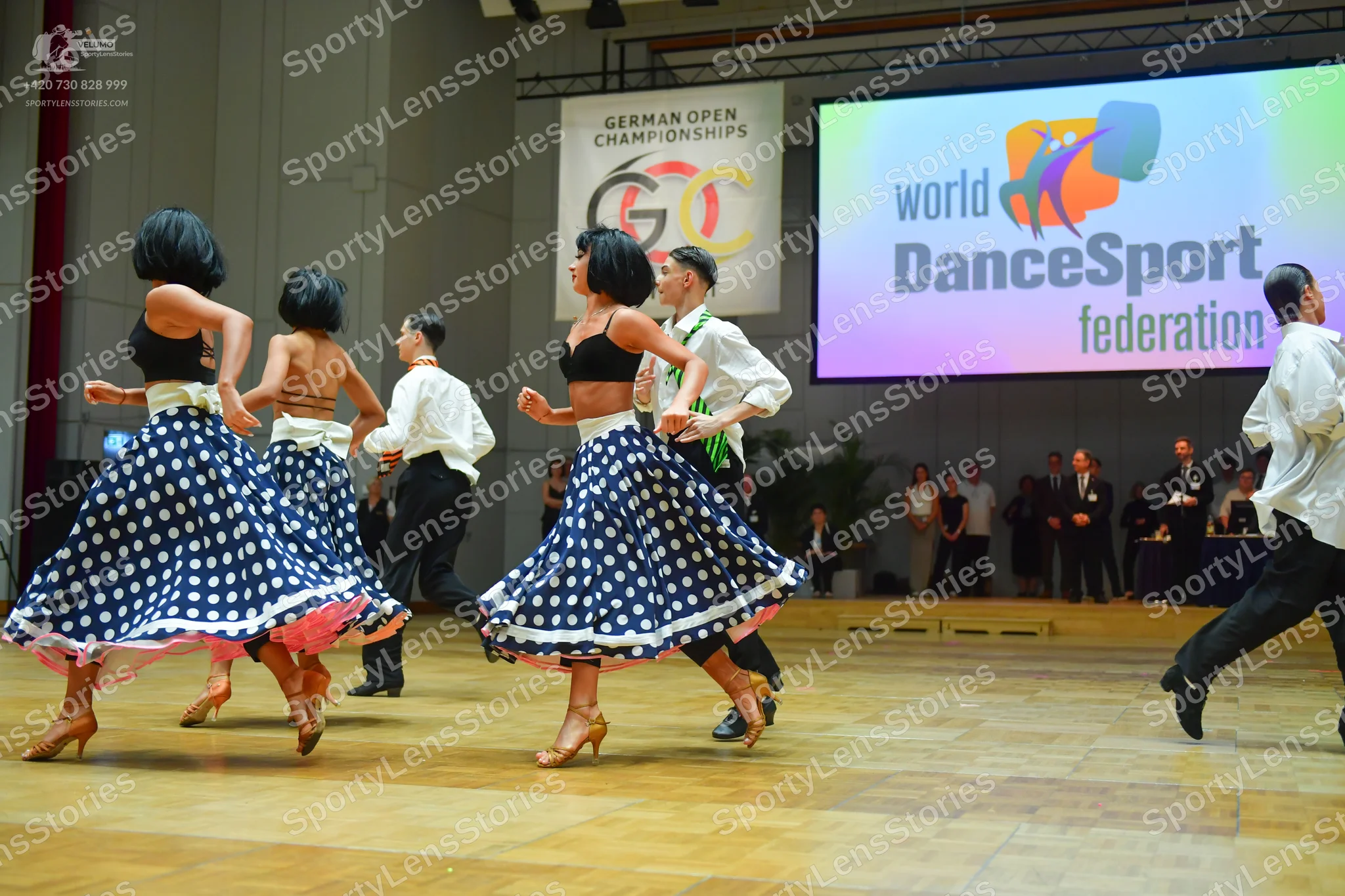 Dancesport competitor: Female dancers: black crop tops with wide white waistbands, and blue skirts with