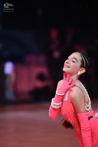 Dancesport competitor: Female dancer: coral pink Latin dance costume with fringe, long matching gloves,