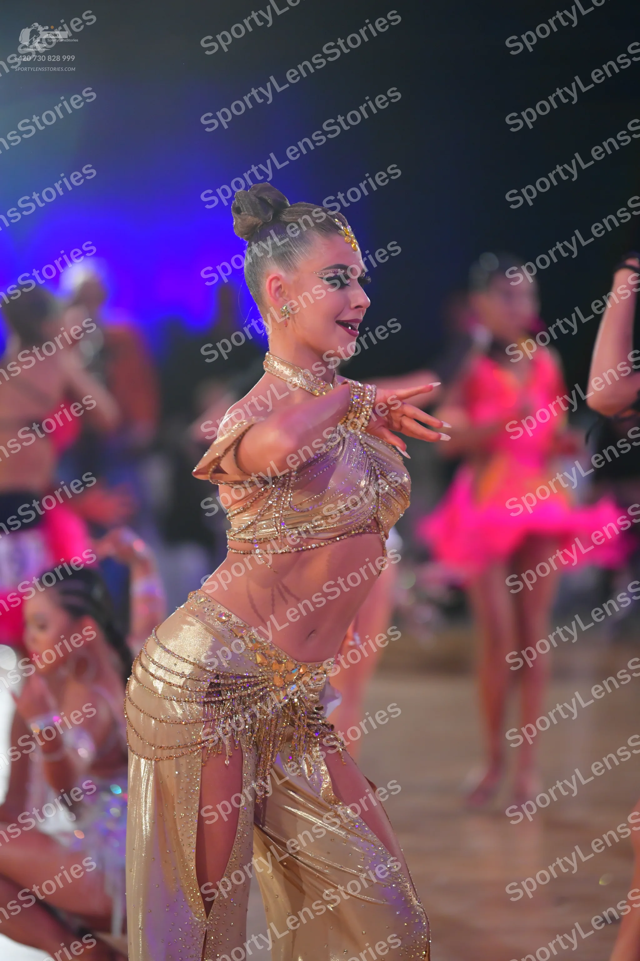 Dancesport competitor: Female dancer in foreground: gold two-piece Latin costume consisting of a sequin